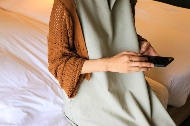 結婚相談所埼玉　スマートフォンを片手にベッドに腰掛ける女性の画像です。