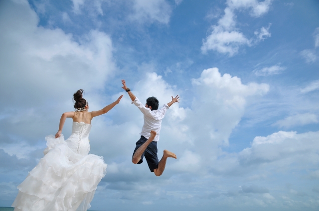 結婚相談所埼玉　青空に向かってジャンプをした瞬間の若い新郎新婦の後ろ姿の画像です。