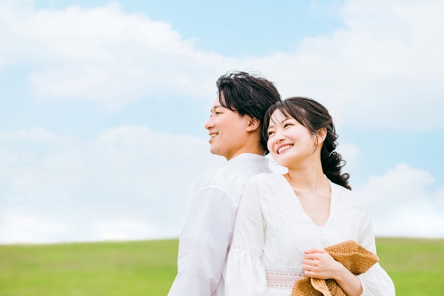 結婚相談所埼玉　青空の元、芝生の上に背中合わせで男女が微笑んで座っている画像です。