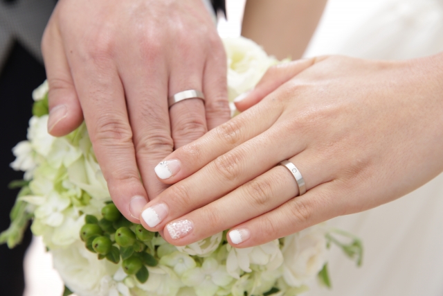 結婚相談所埼玉　結婚指輪をはめた新郎新婦の左手が、少し重なるように白いブーケの上に添えられている画像です。