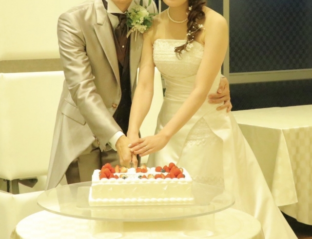 結婚相談所埼玉　結婚披露パーティーで、イチゴが飾られた大きなスクエアケーキにケーキ入刀をしている場面の画像です。
