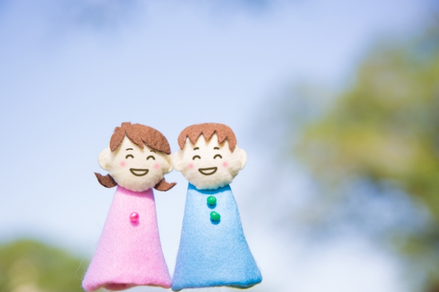 結婚相談所埼玉　フェルトで作られた可愛らしい笑顔の男女の指人形が、屋外で並んで立っているような画像です。