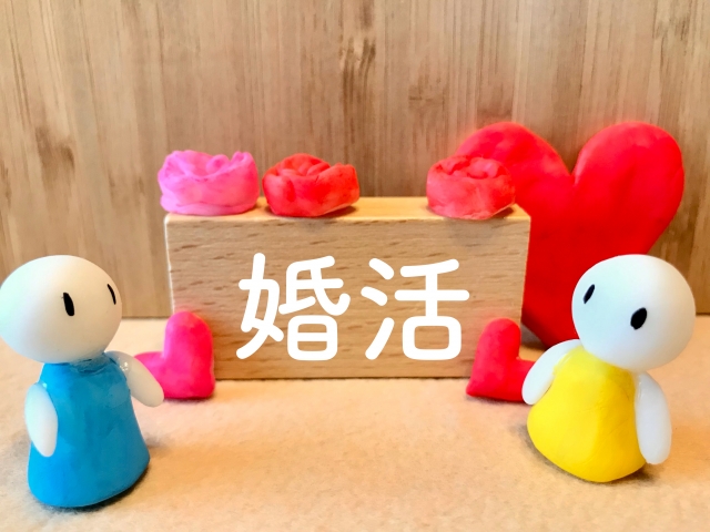 結婚相談所埼玉　男女に見立てた人形が向かい合わせで立っています。真ん中に「婚活」と書かれた木製のブロックやバランスよく粘土のハートが置かれている画像です。